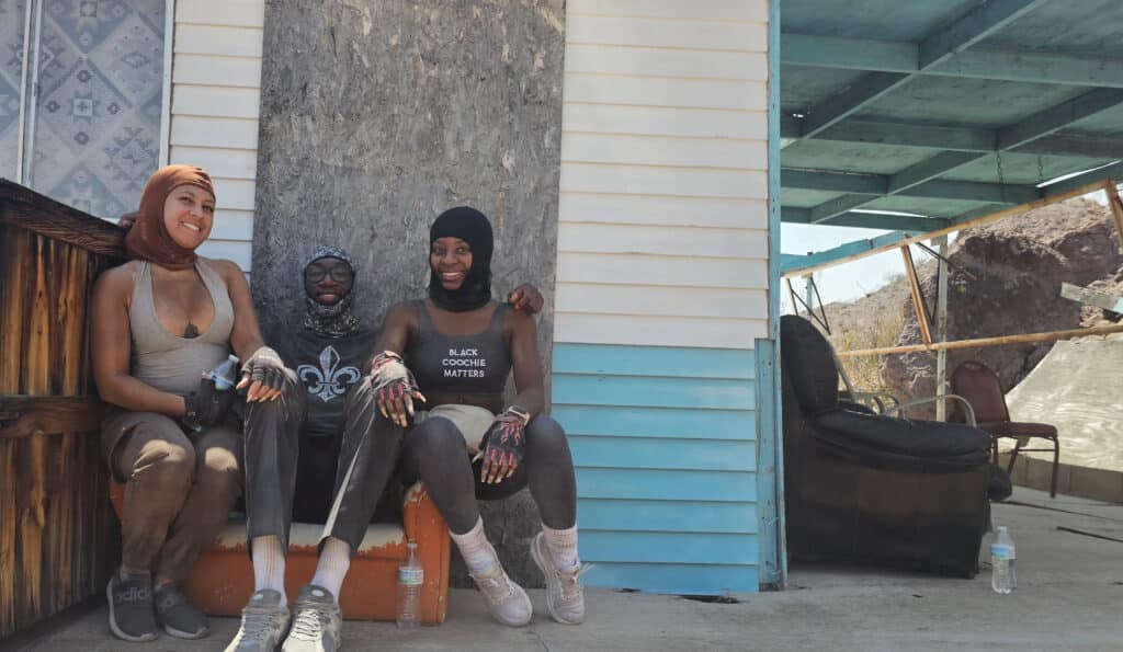 Three friends in headscarves smile on a Nevada porch near the Colorado River, dirt-covered after a Las Vegas ATV tour adventure.