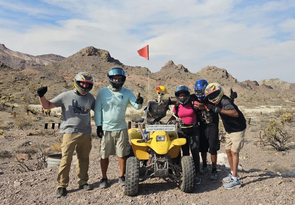 Six adventurers in helmets pose with a yellow ATV in Nevada’s rocky desert near Las Vegas on an exciting Colorado River ATV tour.
