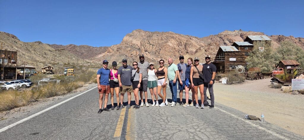 Twelve people on a Nevada desert road near Las Vegas, rustic ghost town, mountains, and old vehicles—perfect for ATV tours.