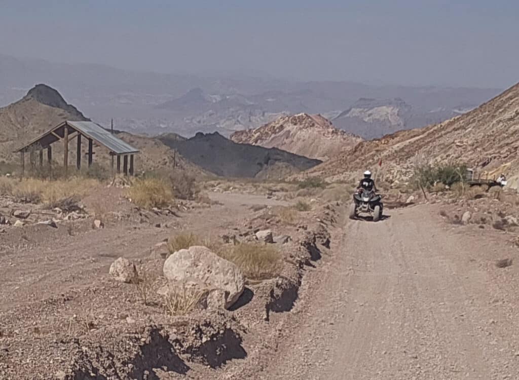 Rider on a motorcycle explores a rocky desert trail near Las Vegas, Nevada, with ghost town sights and rugged hills in the backdrop.