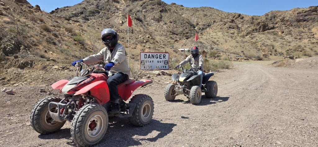 ATV riders explore a rocky Nevada desert trail near Las Vegas; warning sign and helmets highlight safe off-road adventure tours.