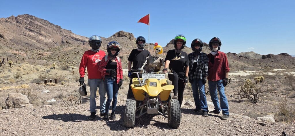 Group in helmets poses with yellow ATV, Nevada desert near Las Vegas, mountains behind. Perfect for ATV tours & off-road adventures.