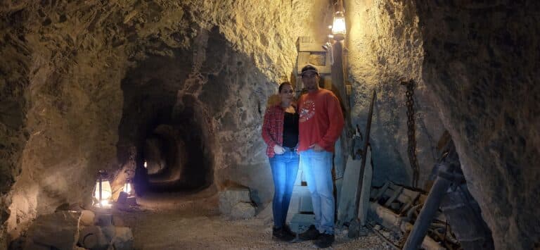 Couple explores a dim cave near Las Vegas, Nevada, lantern-lit with rocky walls and ladder—perfect for Ghost Town sightseeing.