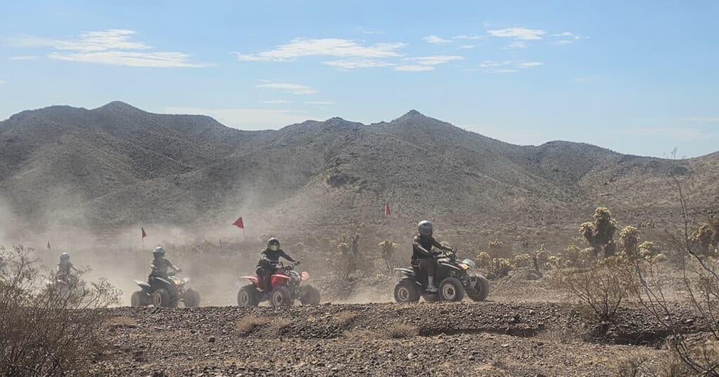 ATV riders with helmets on a Nevada desert trail near Las Vegas, red flags flying, enjoy an off-road RZR tour by the Colorado River.