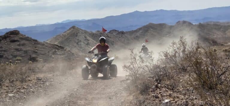 ATV riders explore a dusty Nevada desert trail near Las Vegas with mountains, red flags, and sparse vegetation on an off-road tour.