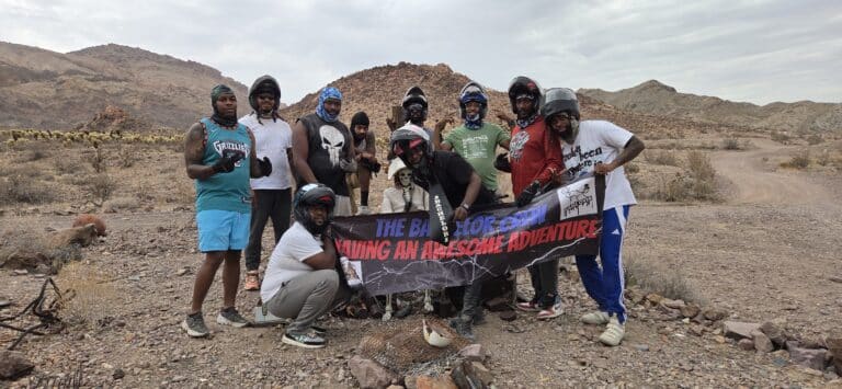 Adventure group and dog pose in Nevada desert near Colorado River after RZR ATV tour, holding “THE B.A.D. BOY CREW” banner.