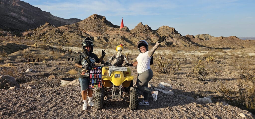 Smiling group on a Las Vegas ATV tour, wearing helmets near Nevada’s rocky desert, posing with “Happy Birthday” sign.