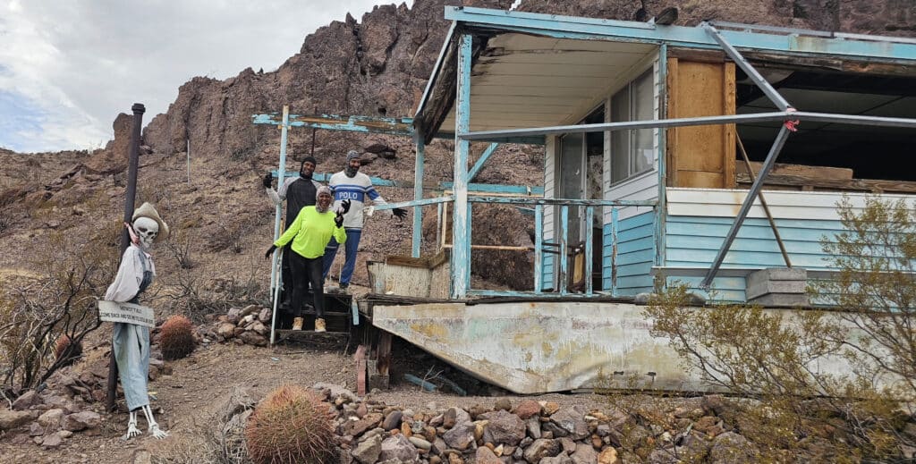 Four people at a rundown trailer in the Nevada desert near Las Vegas; skeleton enjoys Ghost Town sightseeing nearby.