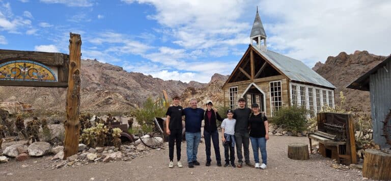 Smiling group at a rustic Nevada ghost town church near Las Vegas with cacti, rocky hills—ideal for Ghost Town sightseeing tours.