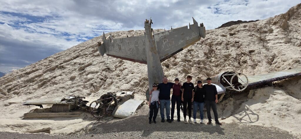 Group of six smiling near a crashed plane in Nevada’s rocky hills, perfect for Las Vegas RZR tours and Ghost Town sightseeing.