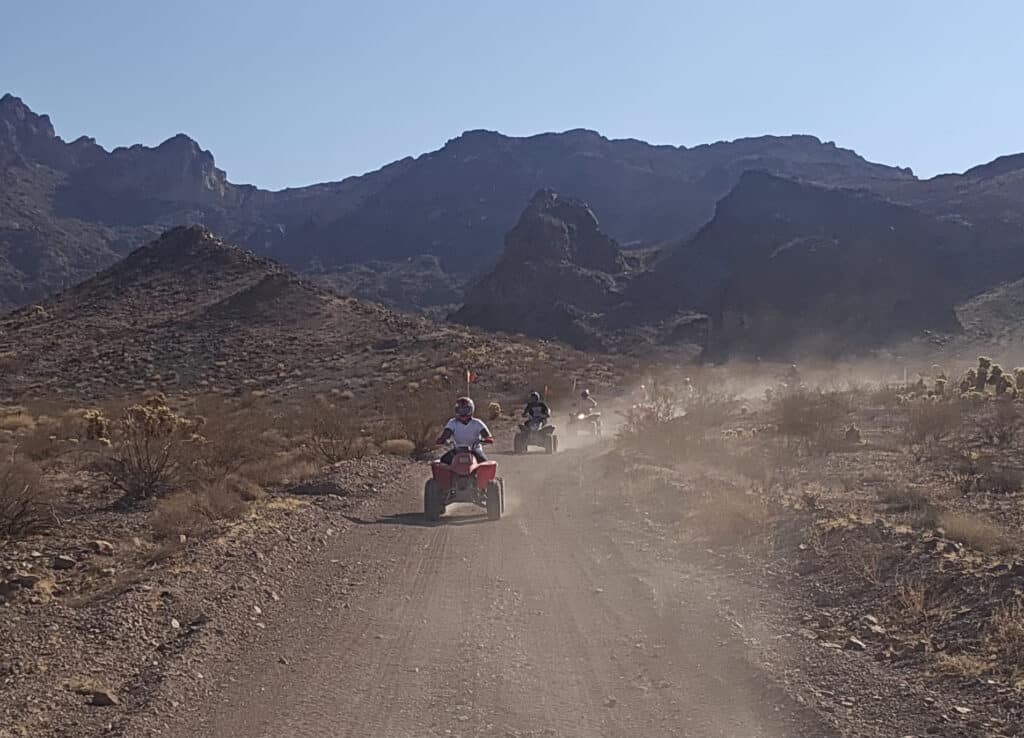 ATV riders explore a dusty Nevada desert trail near Las Vegas with mountain views under clear blue skies, perfect for off-road tours.