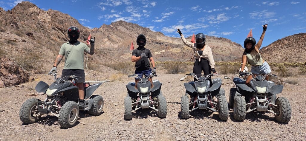 Group on ATVs with helmets in Nevada desert near Las Vegas, celebrating an epic RZR off-road adventure with mountain views.