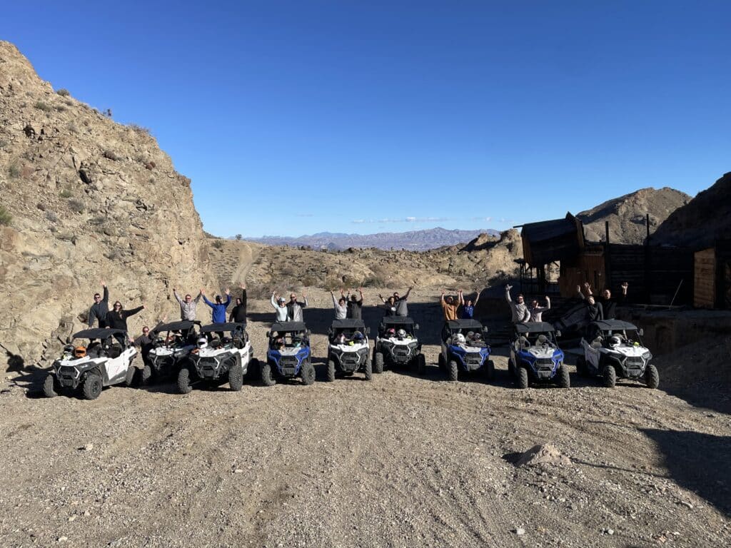 Adventurers celebrate behind ATVs on a Las Vegas ATV tour near the Colorado River, with Nevada desert and Ghost Town views.
