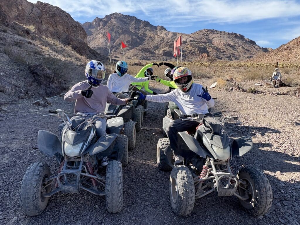 Adventurers in helmets pose by ATVs with red flags in Nevadas rocky desert on a Las Vegas ATV tour near the Colorado River.