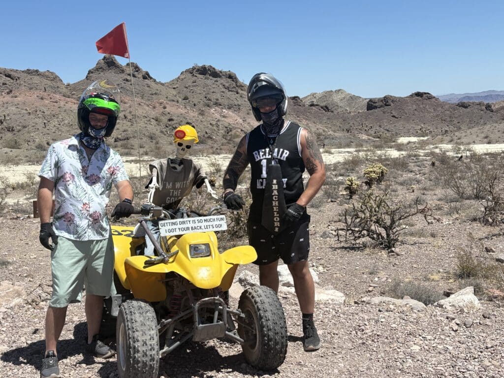Three men in helmets with a skeleton prop pose by a yellow ATV near Las Vegas, Nevada—perfect for Colorado River RZR tours!.