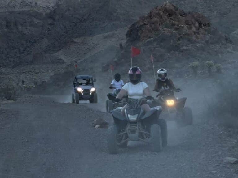 Adventurers ride ATVs near Las Vegas through Nevada’s rocky desert at dusk, red flags flying—perfect for ATV tours or ghost town rides.