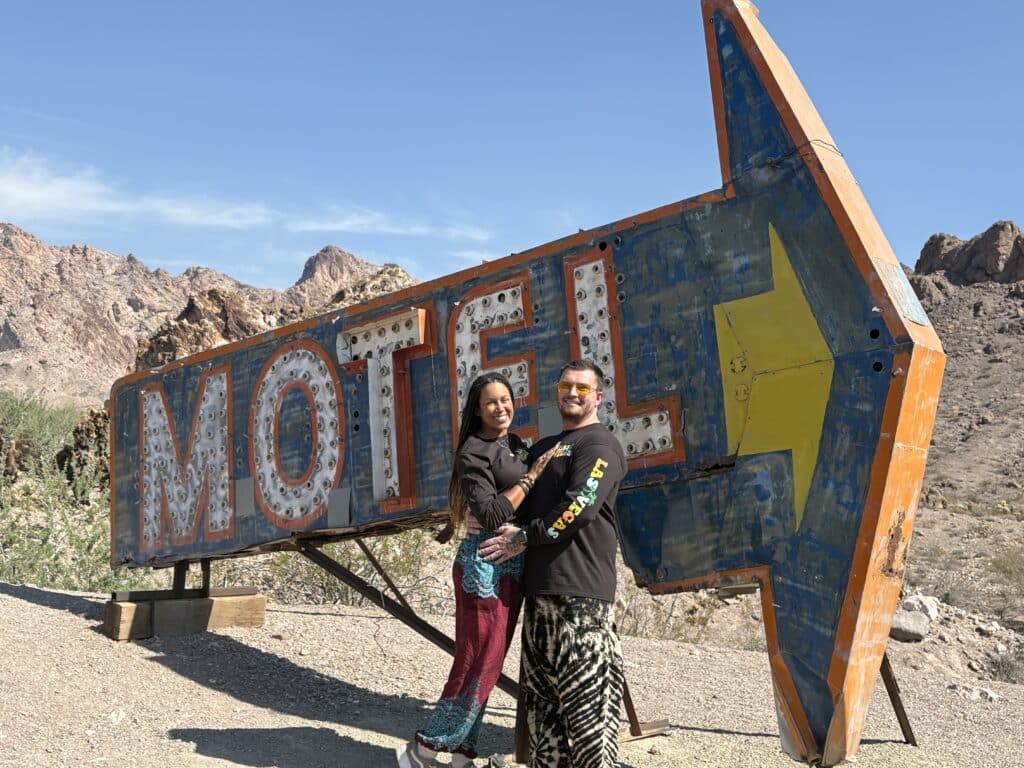 Smiling couple poses by a vintage MOTEL sign in Nevada desert near Las Vegas, perfect for ATV tours & Ghost Town sightseeing.