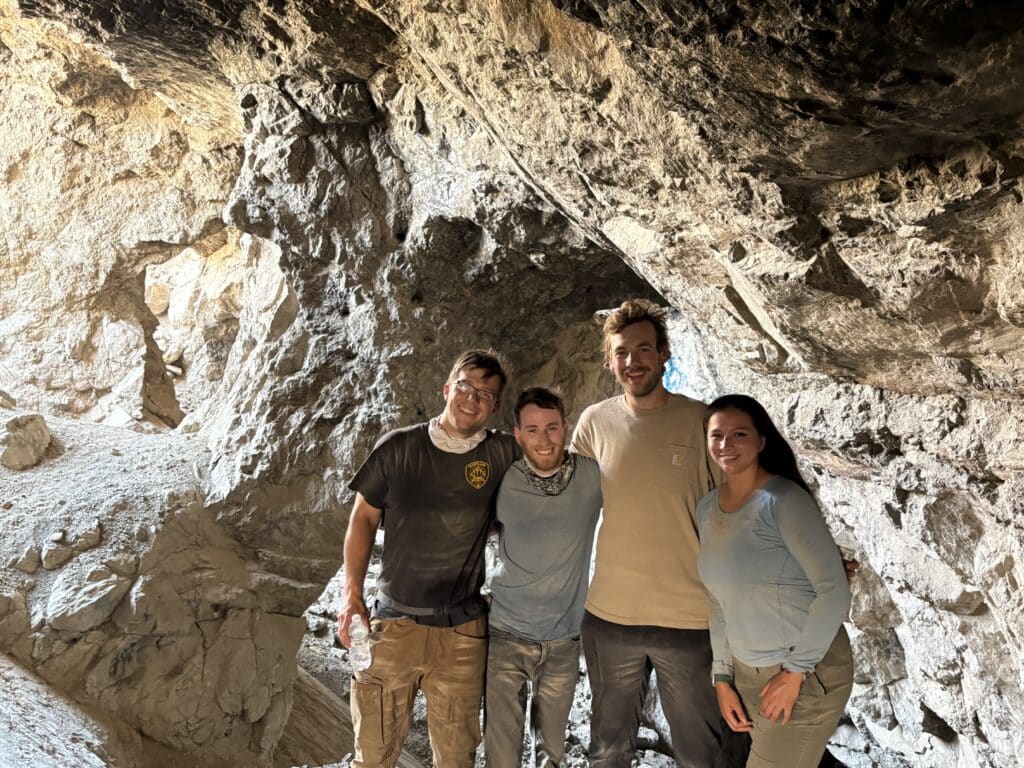 Smiling group in casual attire stands inside a Nevada cave, natural light shining in after Las Vegas ATV tour adventure.
