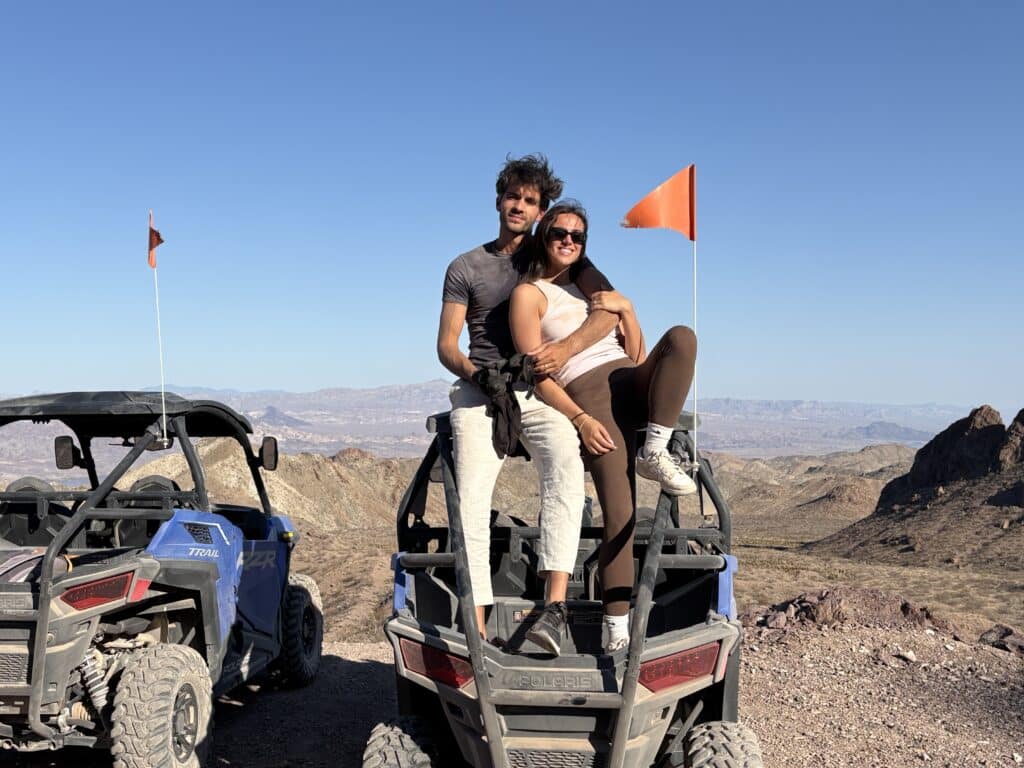 Smiling couple on ATV in Nevada desert near Las Vegas, with mountains and blue sky—perfect for RZR off-road and Ghost Town tours.