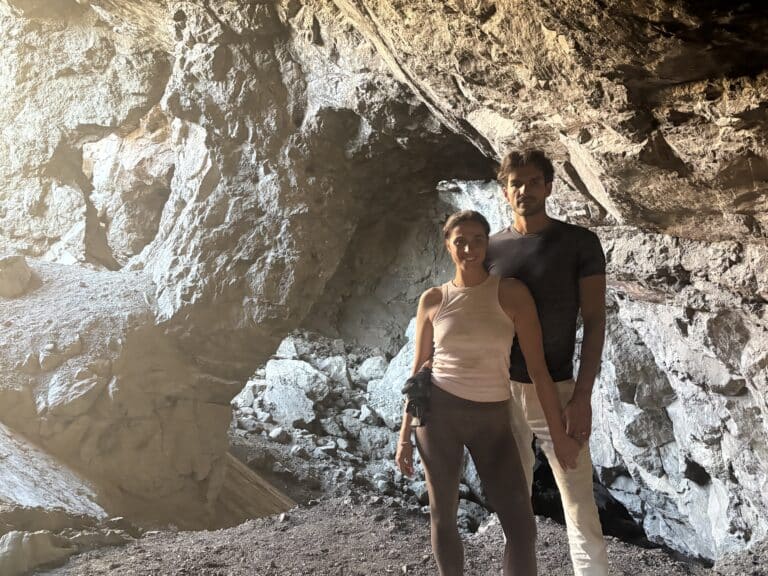 A man and woman stand in a rugged Nevada cave near Las Vegas, sunlight shining in—perfect for RZR tours or Ghost Town sightseeing.