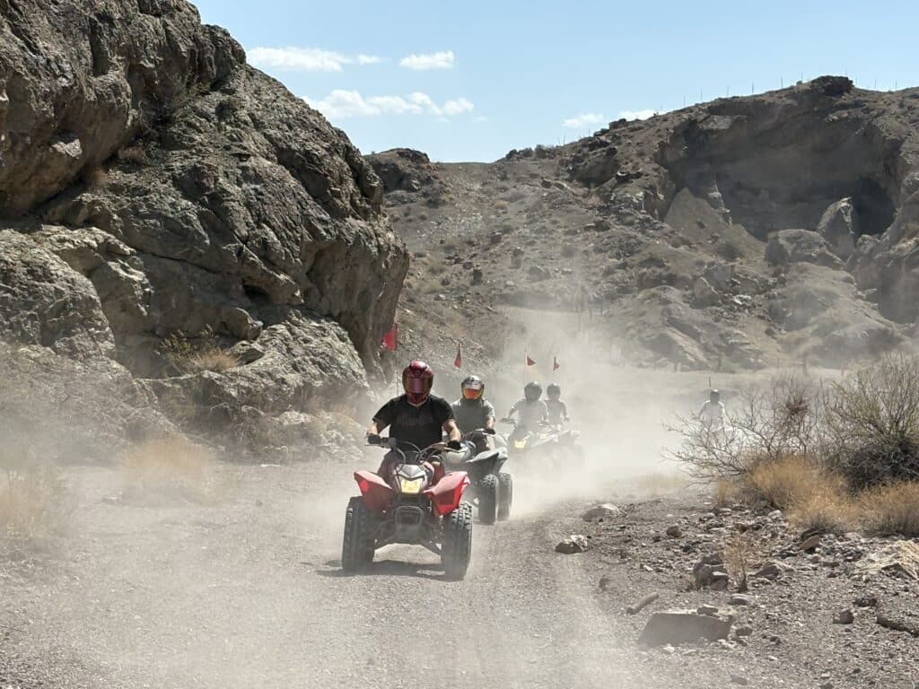 ATV riders explore a dusty desert trail near Las Vegas, Nevada, with rocky cliffs and hills on an exciting off-road tour.