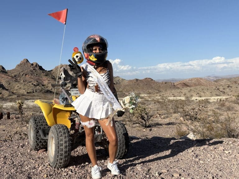 Bride in helmet by yellow ATV in Nevada desert near Las Vegas, holding bouquet; red flag waves—perfect for ATV tours or Ghost Town rides.
