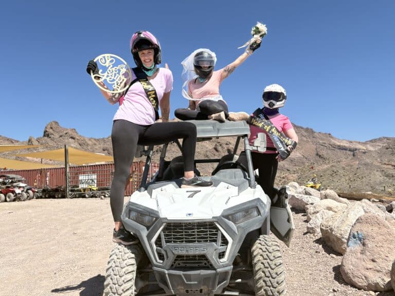Three women in pink and black pose on a Polaris ATV in the Nevada desert, ready for an exciting Las Vegas bachelorette ATV tour.