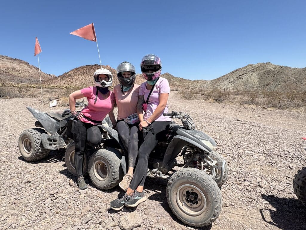 ATV riders in pink shirts explore a rocky Nevada desert near Las Vegas with mountain views on an off-road tour under blue skies.