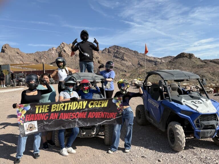 Group posing with a banner during an ATV tour near the Colorado River in Nevada, enjoying Las Vegas adventure activities.