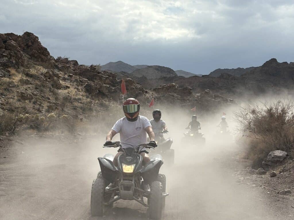 ATV riders explore a dusty Nevada desert trail near Las Vegas, with red flags and mountains—perfect for off-road tours and adventure.