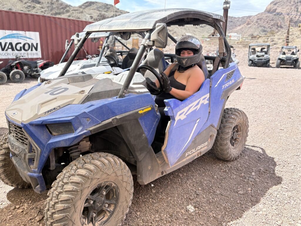Helmeted driver in a blue Polaris RZR tours rocky Nevada terrain near Las Vegas; other off-road vehicles and mountains behind.