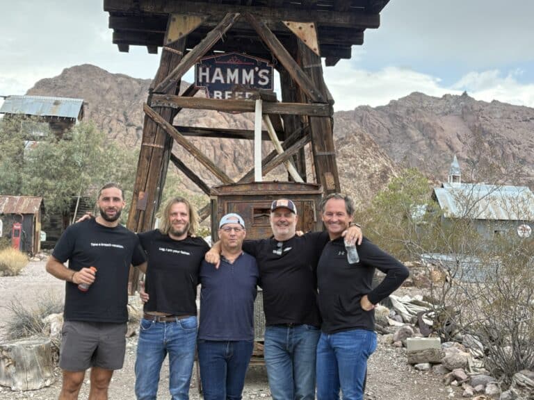 Five men smile under a HAMMS BEER sign at a rustic Nevada ghost town near Vegas, perfect for ATV tours and sightseeing.