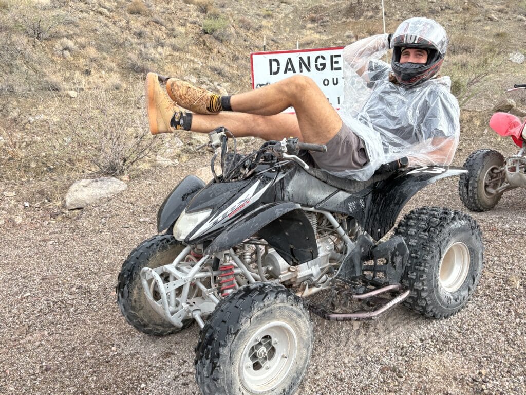 Smiling man in helmet relaxes on ATV during a Las Vegas RZR off-road tour near a Danger sign and rocky Nevada terrain.
