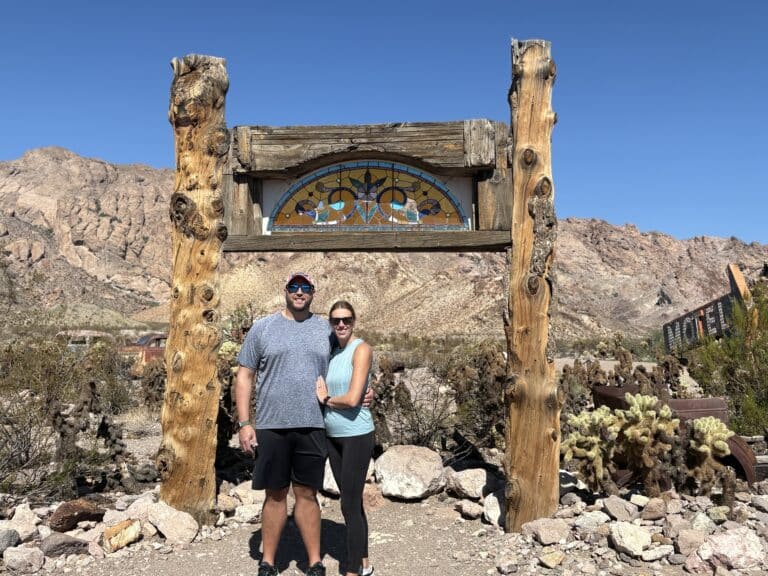 Couple poses under rustic arch with stained glass in Nevada desert near Colorado River, perfect for Las Vegas ATV tours.