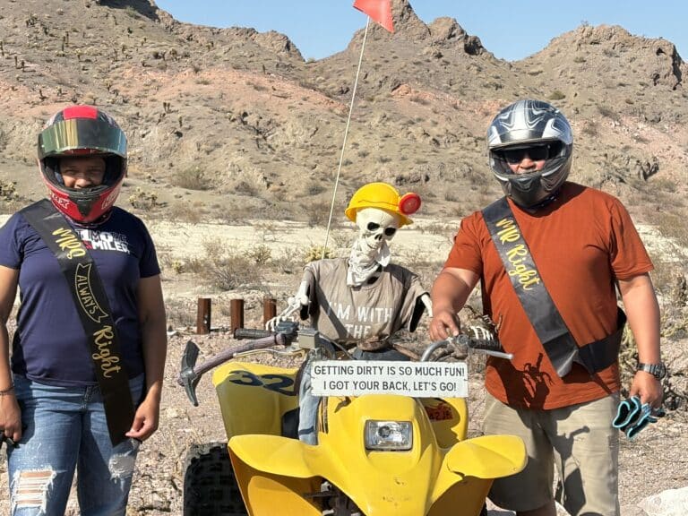 Two people pose by a skeleton on a yellow ATV in Nevada desert, perfect for Las Vegas ATV tours or Ghost Town sightseeing.
