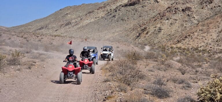 ATV and RZR off-road tours near Las Vegas, Nevada, with riders on red ATVs and utility vehicles on desert trails by rocky hills.