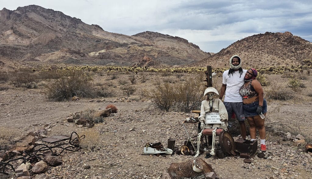 Two people smile in a Nevada desert near Las Vegas, posing by a skeleton at a typewriter—perfect Ghost Town sightseeing shot.