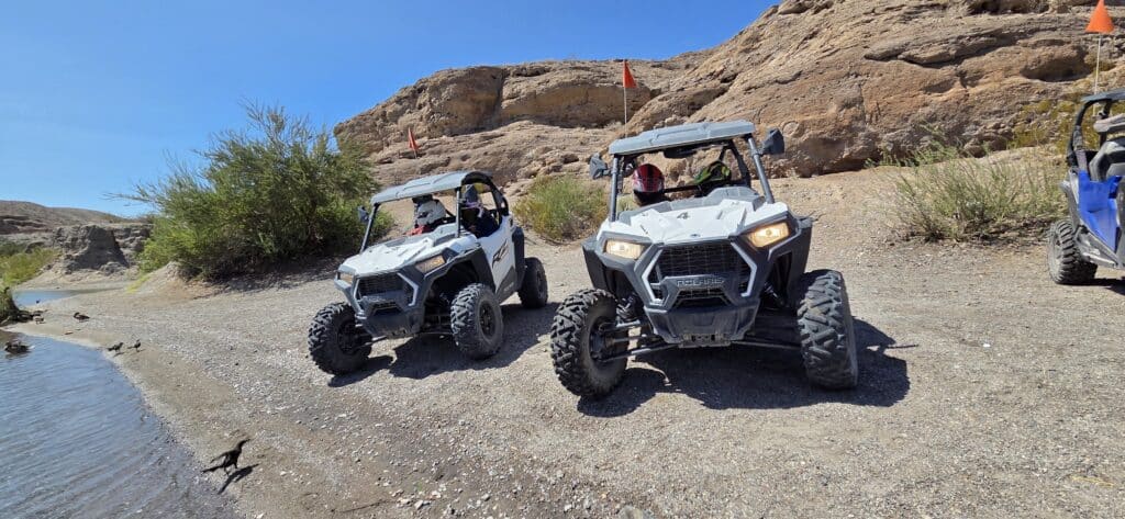 RZR off-road vehicles with roll cages drive along a rocky trail near the Colorado River in Nevada on a Las Vegas ATV tour.