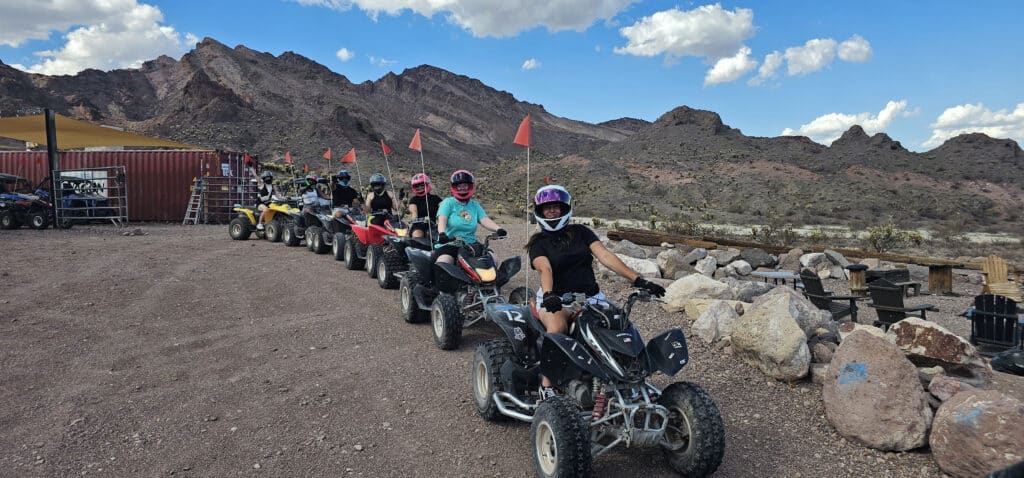 Helmeted riders on ATVs line up for a thrilling Nevada desert ATV tour near Las Vegas with mountains and blue sky behind.