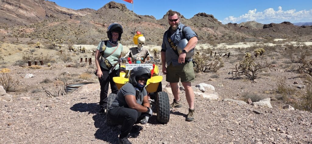 Three people and a mannequin with a yellow ATV in the Nevada desert near Las Vegas, perfect for ATV tours and Ghost Town sightseeing.