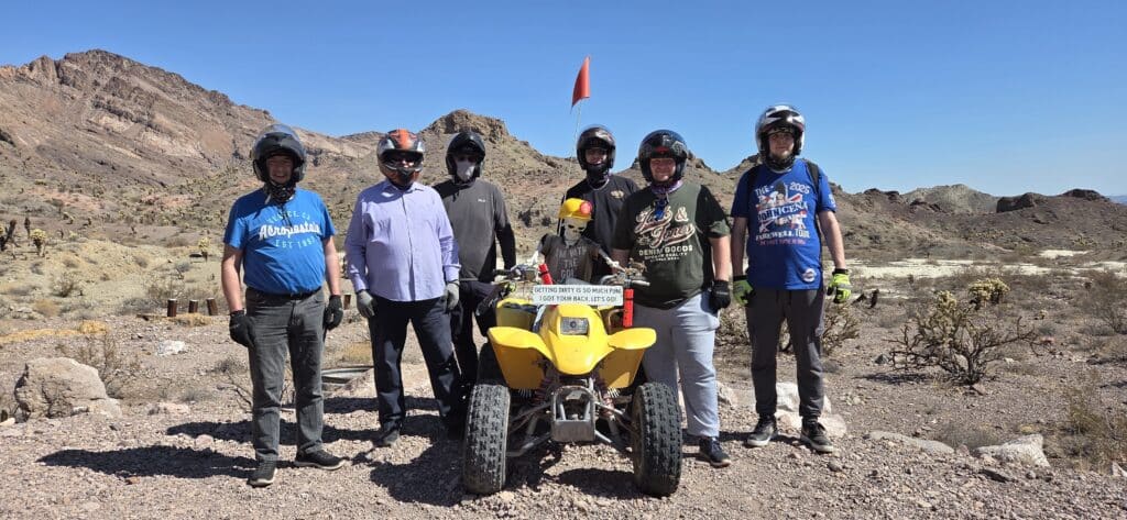 Six people in helmets by a yellow ATV in Nevada desert near Las Vegas, ready for an exciting RZR off-road tour under blue skies.