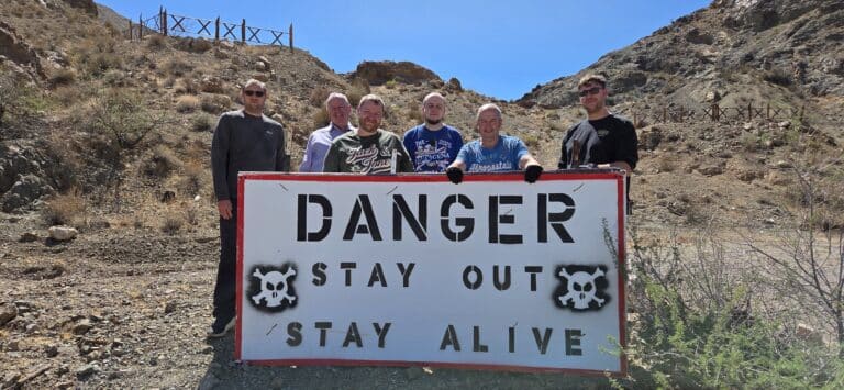 Six people near Las Vegas in a rocky Nevada desert hold a “DANGER STAY OUT STAY ALIVE” sign—ideal for ATV or RZR tour safety.