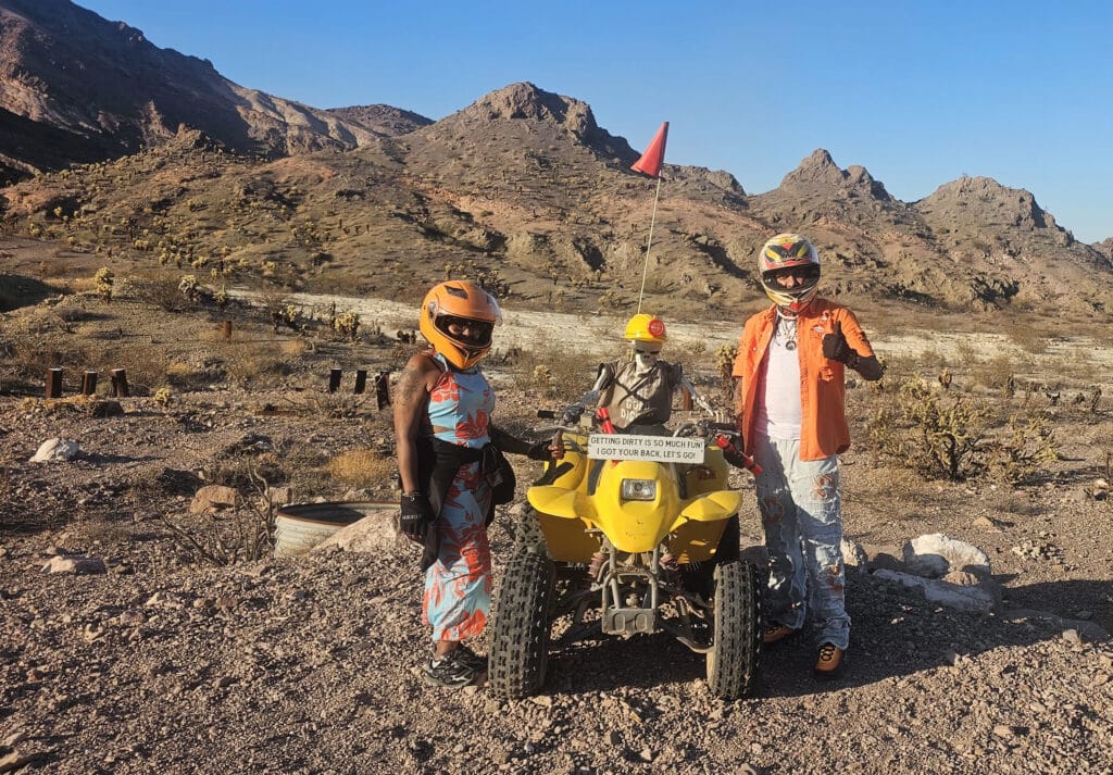Riders in helmets pose by a yellow ATV on Nevada terrain near Las Vegas, perfect for RZR off-road tours and desert adventures.