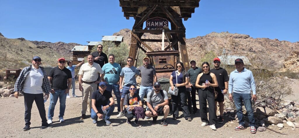 Group posing in front of HAMM'S COFFEE in a Nevada ghost town near Las Vegas, ready for ATV tours under clear blue skies.