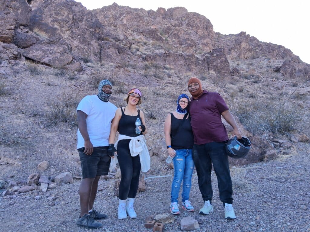 Group enjoys ATV tour near Las Vegas on a rocky desert trail, wearing bandanas, with brown Nevada hills and one holding a helmet.