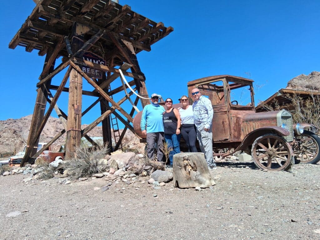 Group poses by a vintage car and old mining structure in Nevada desert near Las Vegas—perfect for Ghost Town sightseeing tours.