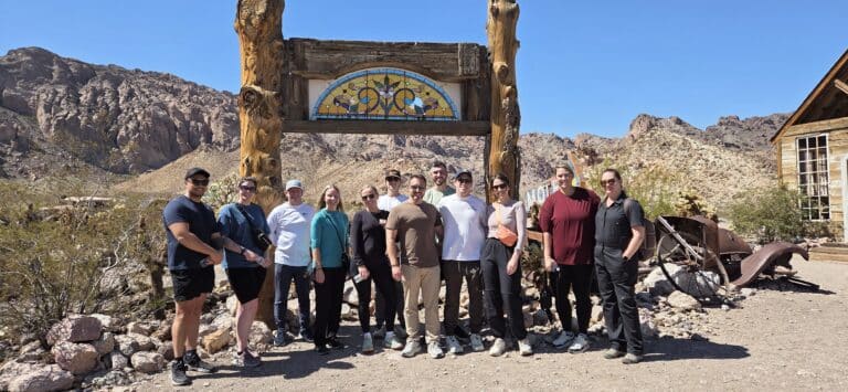 Smiling group at rustic archway in Nevada desert near Las Vegas, with mountains—perfect for ATV tours and Ghost Town sightseeing.