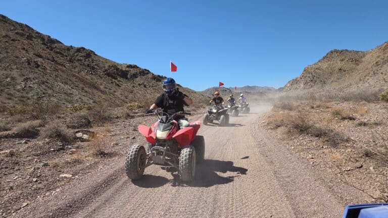ATV riders explore a dusty desert trail near Las Vegas and the Colorado River, with red flags waving in the Nevada sun.