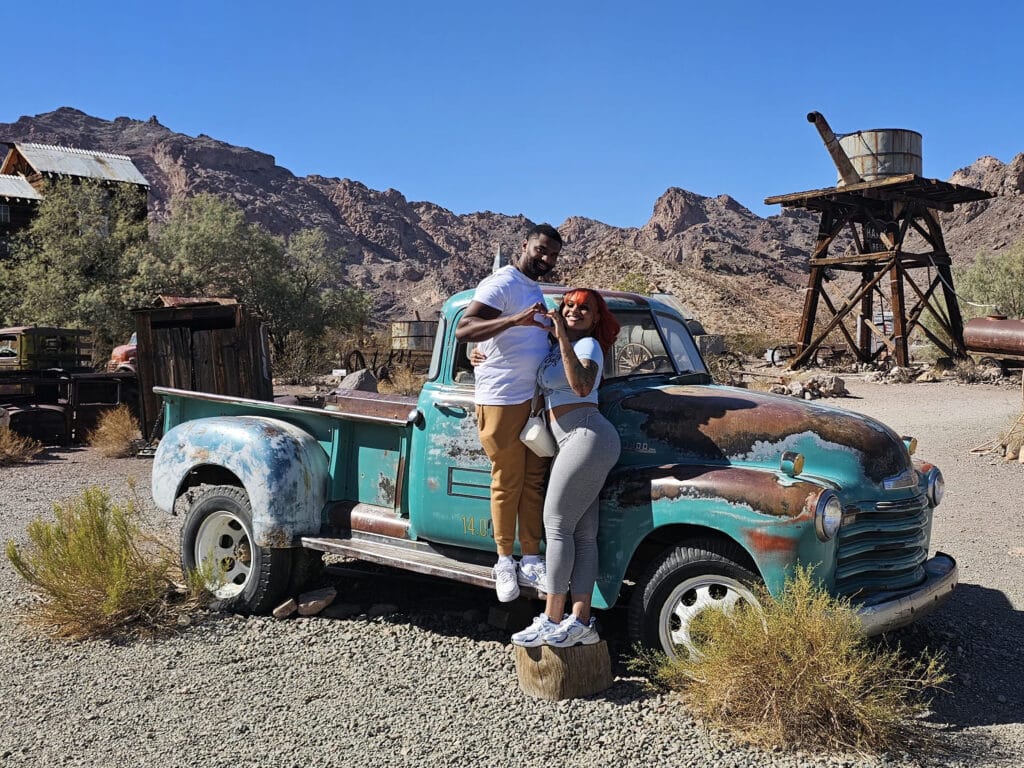 Smiling couple in front of a vintage truck at a Nevada ghost town near Las Vegas, perfect for sightseeing and ATV tours.