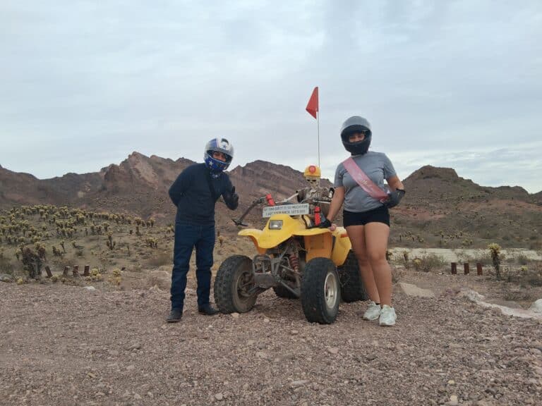 Adventurers in helmets pose by a yellow ATV on a Nevada desert trail near Las Vegas, perfect for ATV tours and RZR rides.